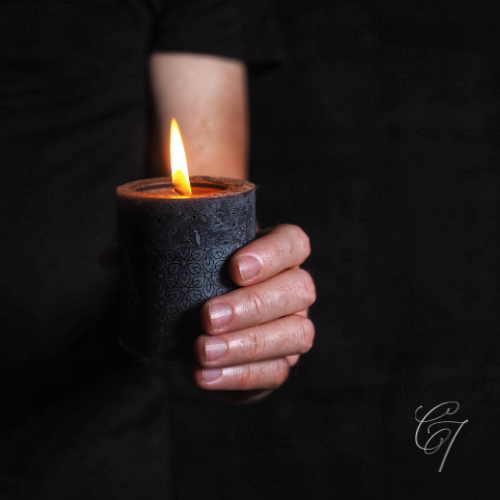Hand holding lit candle agains dark background